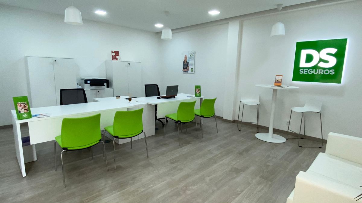 Interior da agência DS Seguros em Buarcos: secretárias brancas, cadeiras verdes e o logótipo DS Seguros iluminado na parede.
